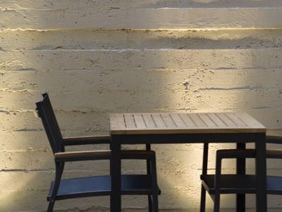 Stół i krzesło na zewnątrz przed oświetloną betonową ścianą z logo hotelu.