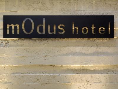 Panneau noir avec inscription dorée 'modus hotel' sur un mur couleur sable.
