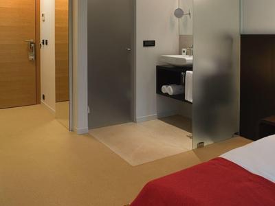 Nowoczesny pokój hotelowy z otwartą łazienką i czerwonym narzutem na łóżko.