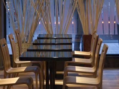 Nowoczesna jadalnia z wieloma stołami, krzesłami i dekoracyjnymi drewnianymi patyczkami przed dużymi oknami.