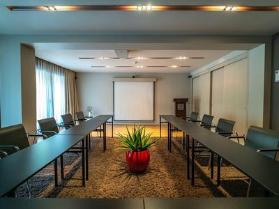 Nowoczesna sala konferencyjna z dwoma długimi stołami, krzesłami i ekranem projektora.