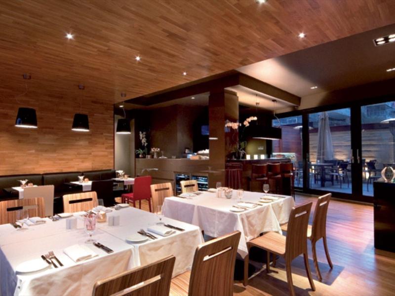 Nowoczesna restauracja z drewnianymi ścianami i nakrytymi stołami, widok na taras z miejscami do siedzenia.