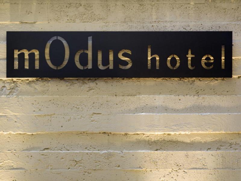 Czarna tablica z złotym napisem "mOdus hotel" na beżowej ścianie.