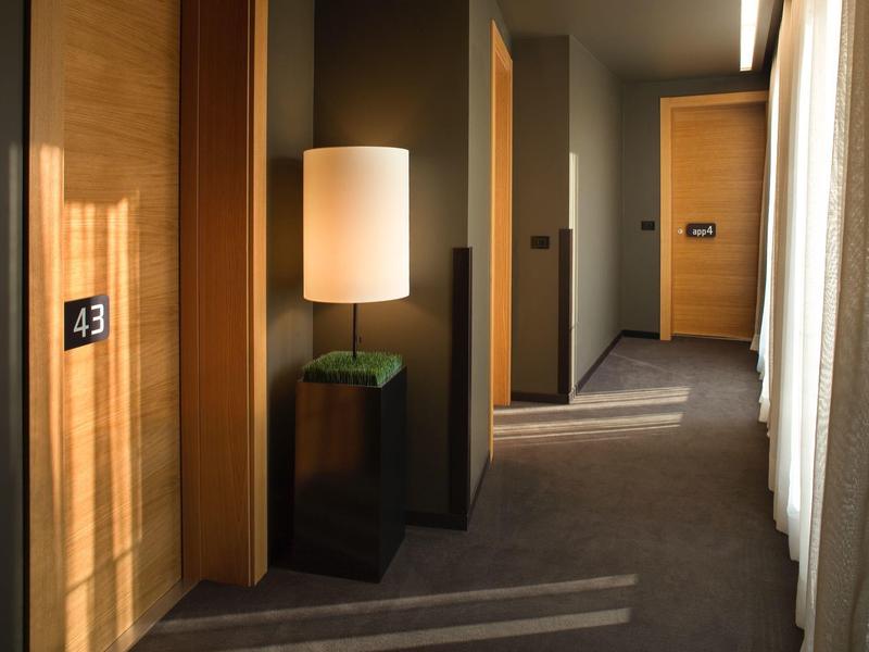 Korytarz hotelowy z drewnianymi drzwiami, wykładziną i lampą podłogową obok drzwi nr 43.