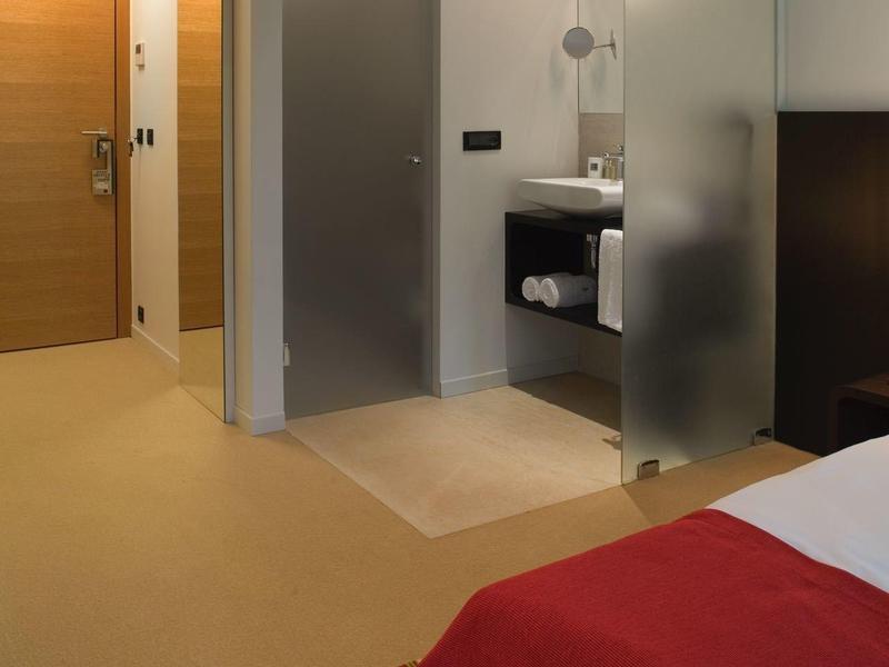 Nowoczesny pokój hotelowy z otwartą łazienką i czerwonym narzutem na łóżko.