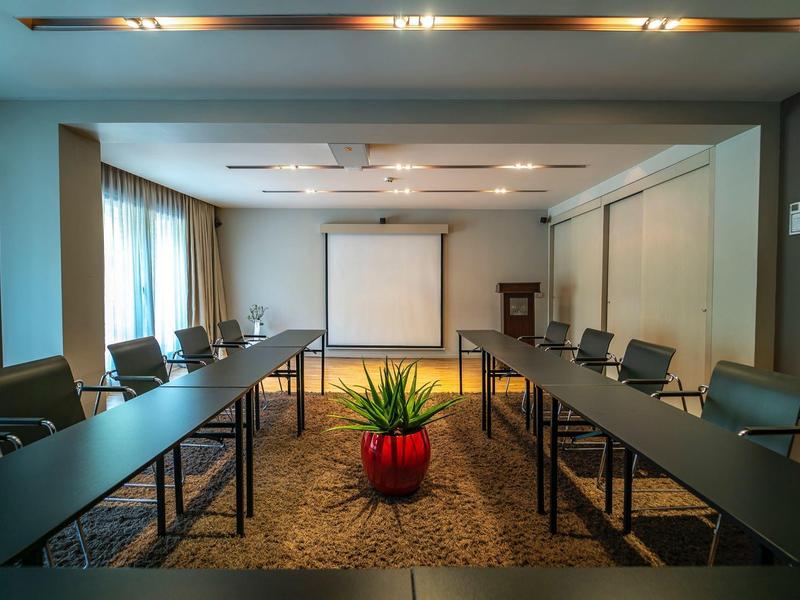 Nowoczesna sala konferencyjna z dwoma długimi stołami, krzesłami i ekranem projektora.