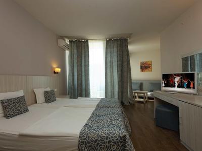 Brightly furnished hotel room with double bed, TV, and curtains over the window.