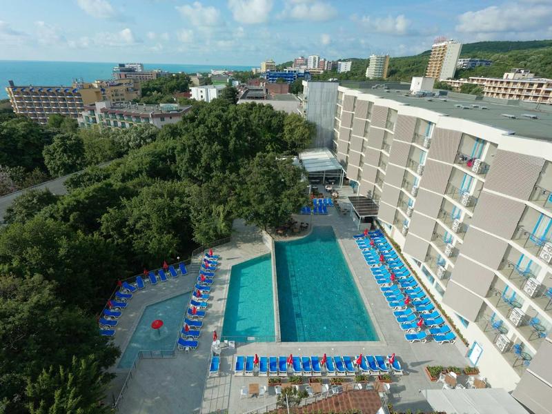 Large hotel with outdoor pool, surrounded by sun loungers overlooking the sea.