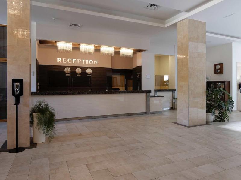 Elegant hotel reception with large front desk, bright marble columns, and plants.
