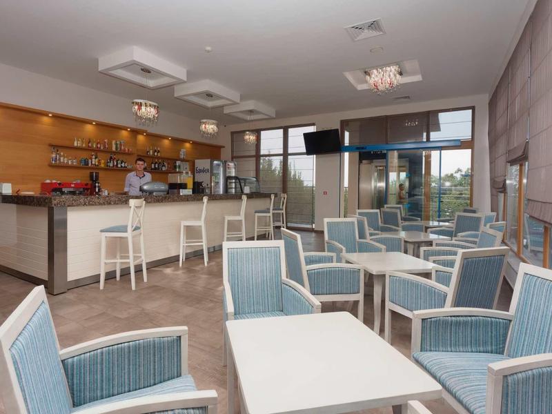 Modern hotel bar area with white tables, blue armchairs, and a counter with stools.
