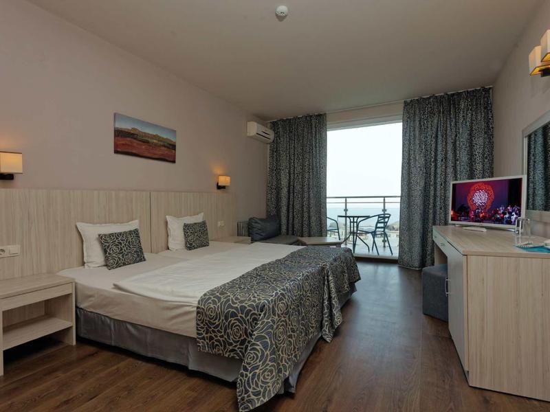 Bright hotel room with two beds, balcony, and sea view