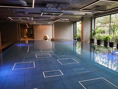 Modern indoor pool with blue tiles and large windows overlooking greenery.