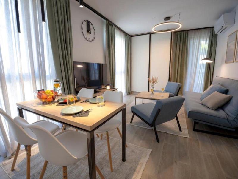 Modern living room with dining area, sofa, armchairs, and large windows with curtains.