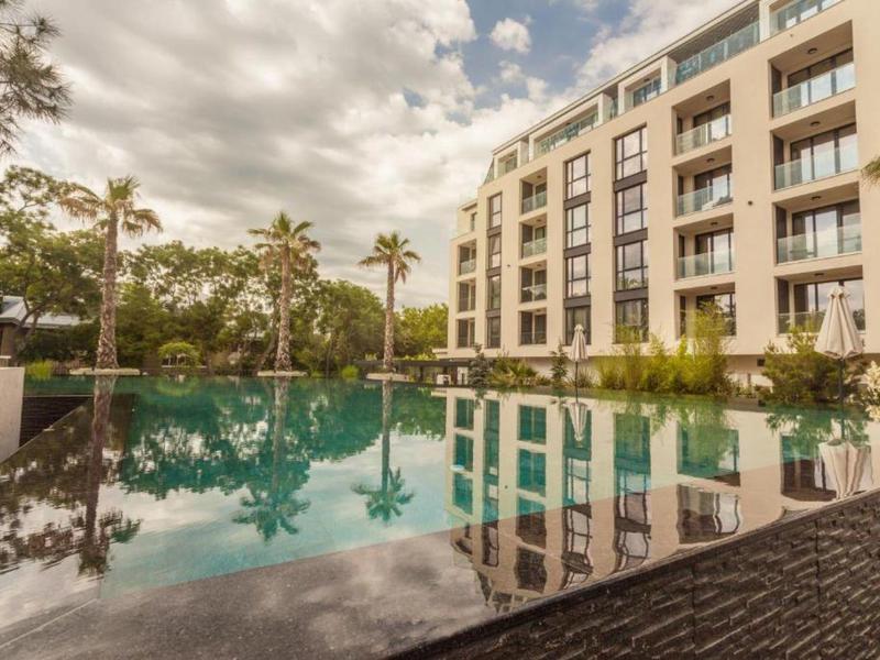 Modern hotel complex with swimming pool and palm trees under a cloudy sky.