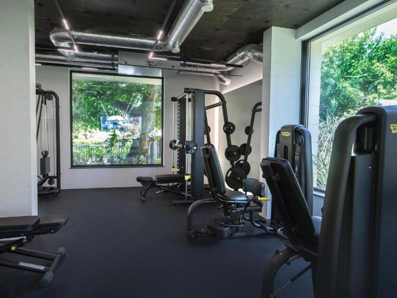 Bright gym with modern equipment and large windows overlooking trees.