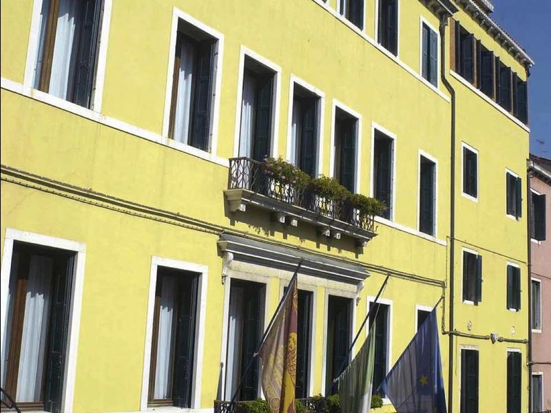 Yellow three-story building with flags and multiple windows under clear blue sky