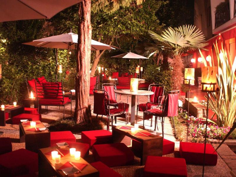 Cozy outdoor lounge with red seating, candles, and large umbrellas at night.
