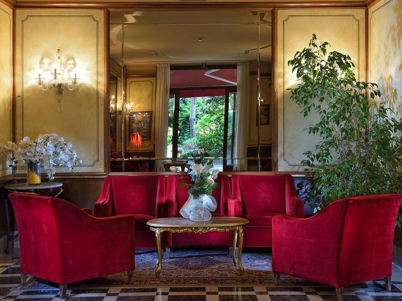 Elegant lounge with red velvet chairs, gold table, and large mirrors.