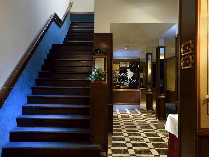 Interior of a hotel with dark wooden staircase and checkered floor in the lobby area.