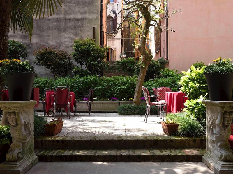 Cozy terrace with tables and chairs surrounded by green plants and buildings.