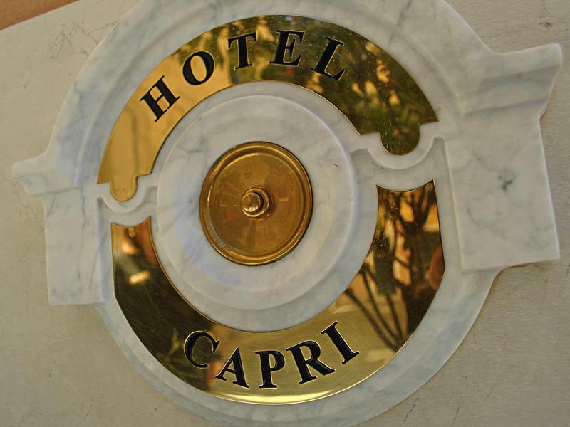 Golden and white round hotel sign with the inscription Hotel Capri on a wall.
