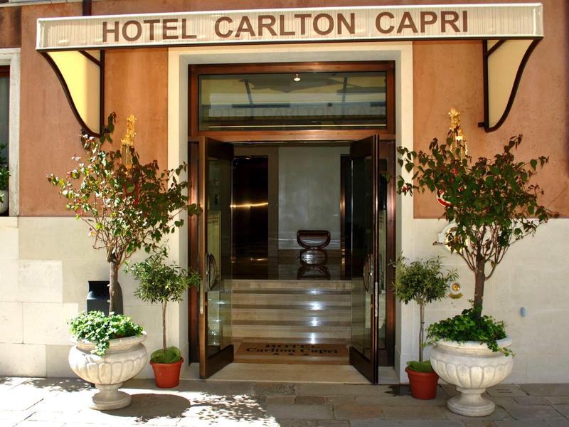 Entrance of Hotel Carlton Capri with glass door and plants on both sides.
