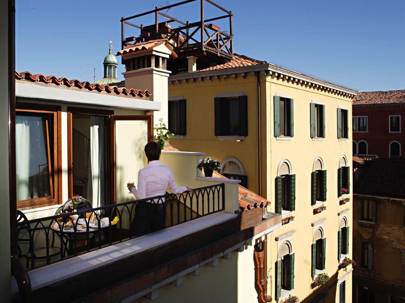 View of a hotel terrace with a waiter and charming historic buildings under clear sky.
