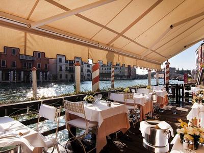 Restaurant terrace by the water with set tables and view of historic buildings.