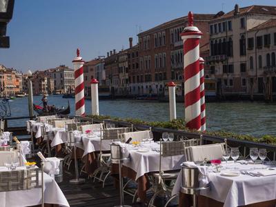 Restaurant terrace by the canal with white tablecloths and red-and-white striped poles
