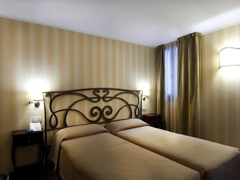 Hotel room with two single beds, decorative headboard, and soft lighting.