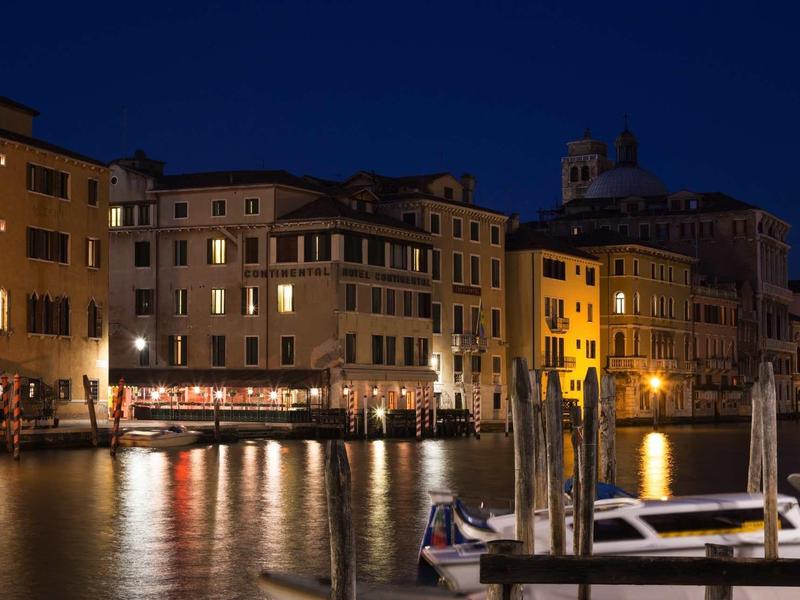 Night view of a Venetian canal with illuminated buildings and boats.