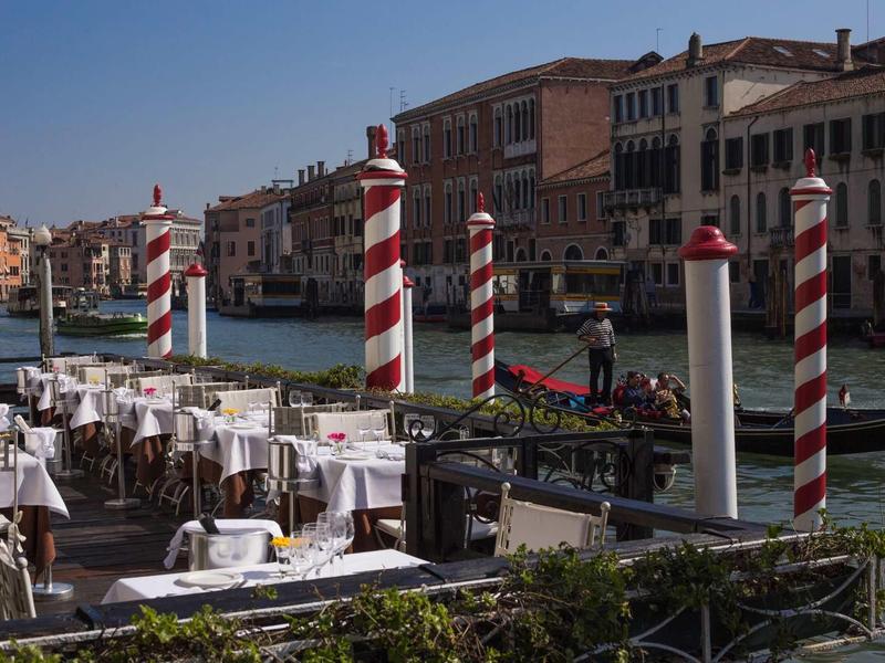 Outdoor dining with set tables along the Grand Canal in Venice on a sunny day.