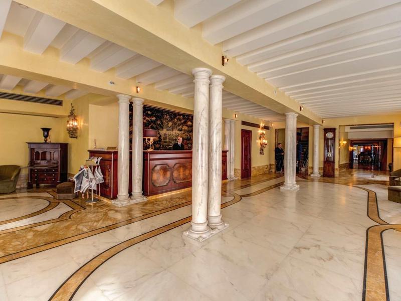 Spacious hotel lobby with marble floor, columns, and warm-colored reception desk.
