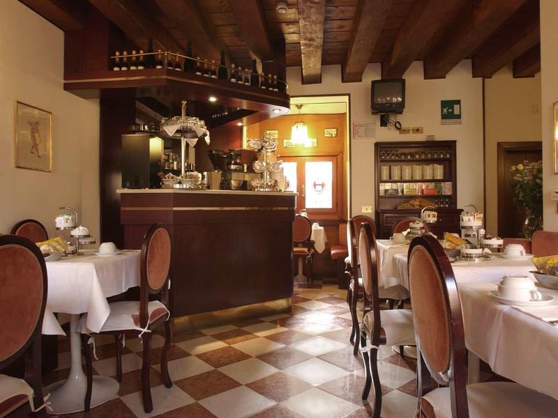 Restaurant cosy avec plafond à poutres en bois, chaises rondes et tables dressées sous une lumière chaude.