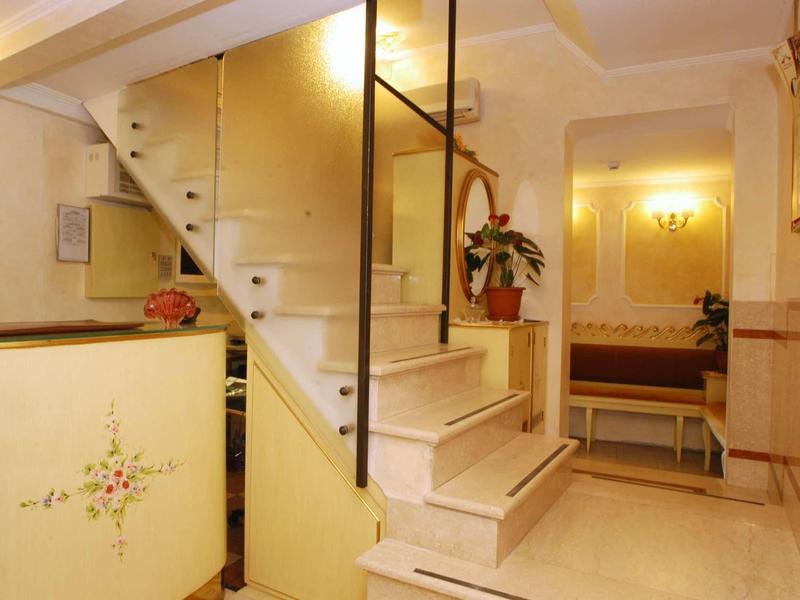 Hall d'hôtel lumineux avec escalier, plante et coin salon en arrière-plan.