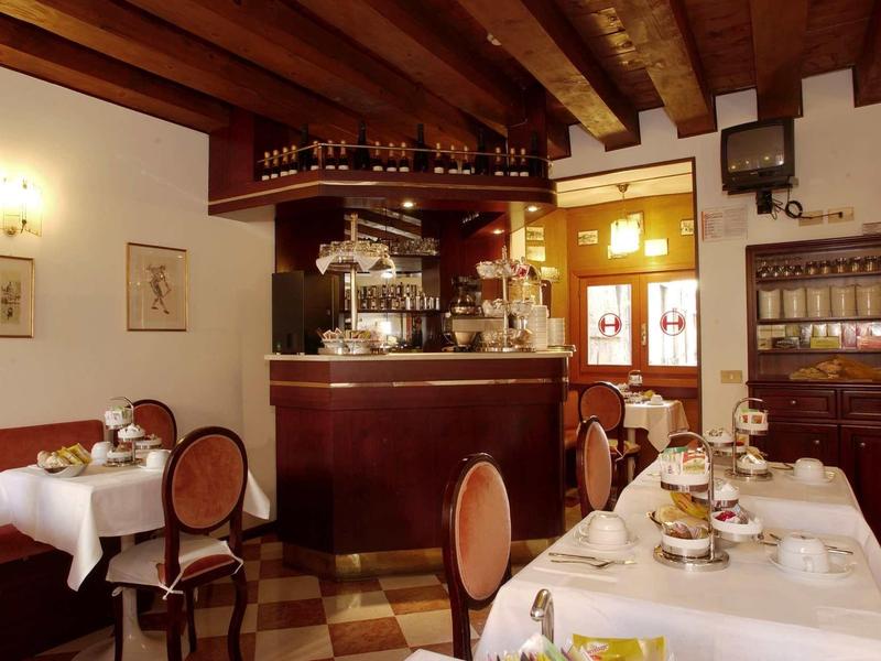 Salle de petit-déjeuner cosy avec tables dressées, plafond en bois et machine à café au comptoir.