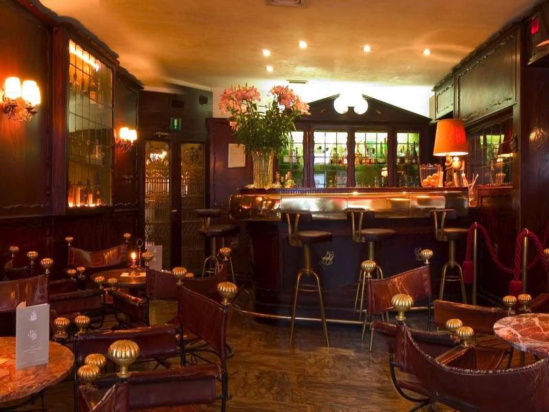 Przytulny bar hotelowy z ciemnego drewna, ciepłym światłem i kilkoma stolikami.