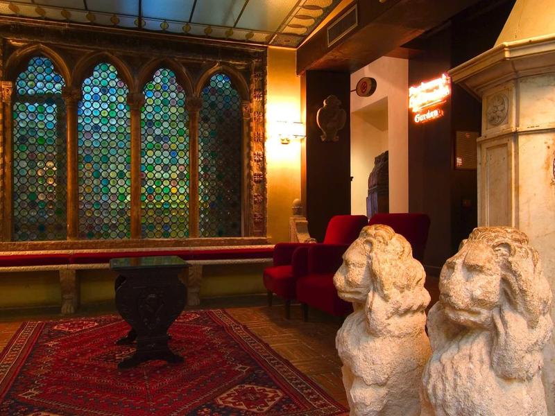 Elegancka hotelowa lobby z witrażami, czerwonymi fotelami i kamiennymi rzeźbami lwów.