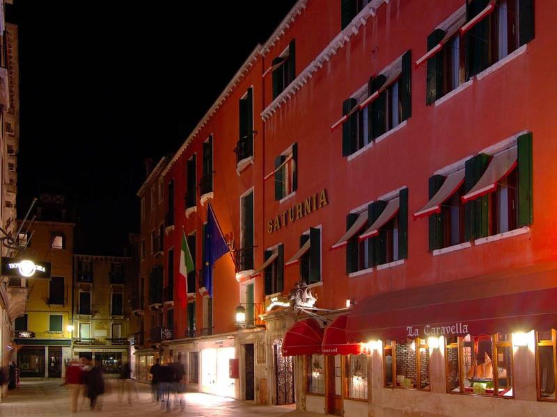 Nocny widok oświetlonego hotelu z czerwonymi markizami na cichej ulicy.