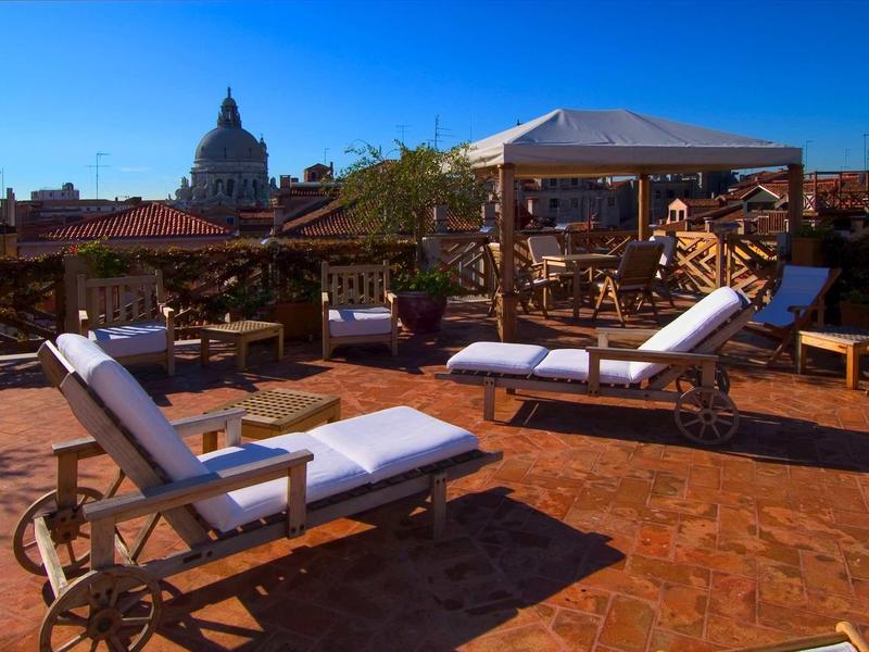 Taras z leżakami i parasolem na tle historycznego miasta przy bezchmurnym niebie.