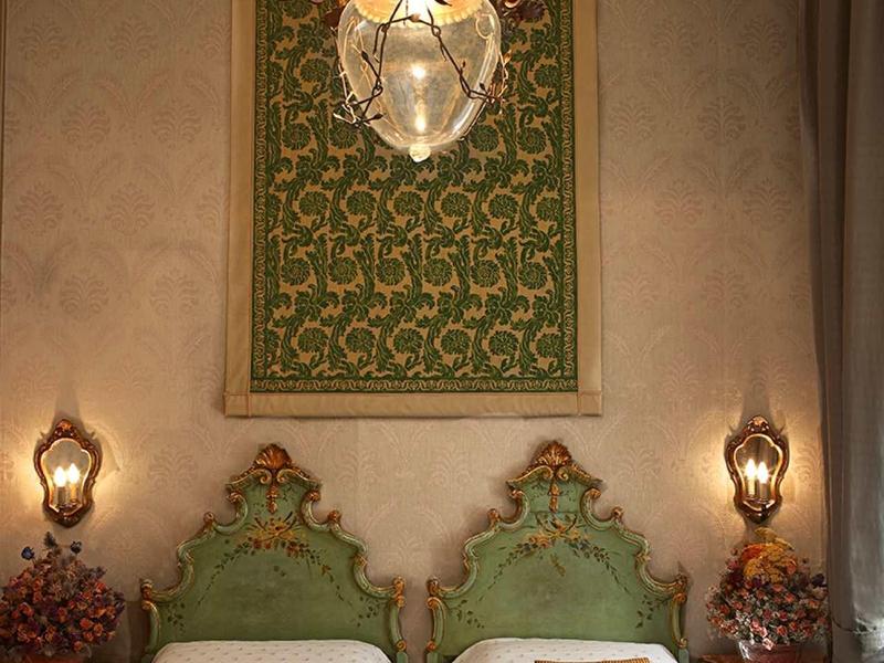 Dwa pojedyncze łóżka z zielonymi ozdobnymi zagłówkami i żyrandolem w eleganckim pokoju hotelowym.