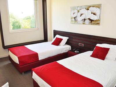 Ein einfach eingerichtetes Zimmer mit zwei Einzelbetten, weißen Bettdecken und roten Akzenten.