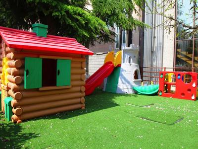 Kinderspielplatz mit Holzhütte, Rutsche und Klettergerüst auf grünem Kunstrasen.