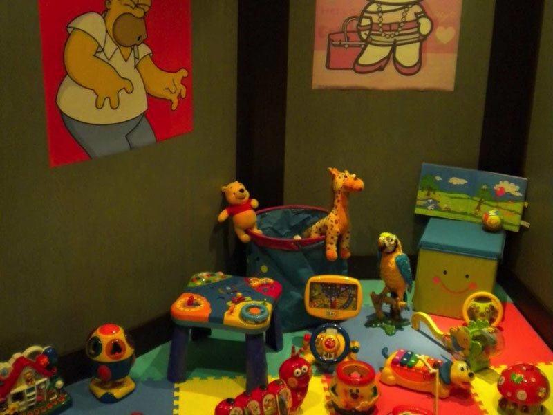 Kinderzimmer mit bunten Spielzeugen, Tieren und Figuren auf blauem Boden vor bemalten Wänden.