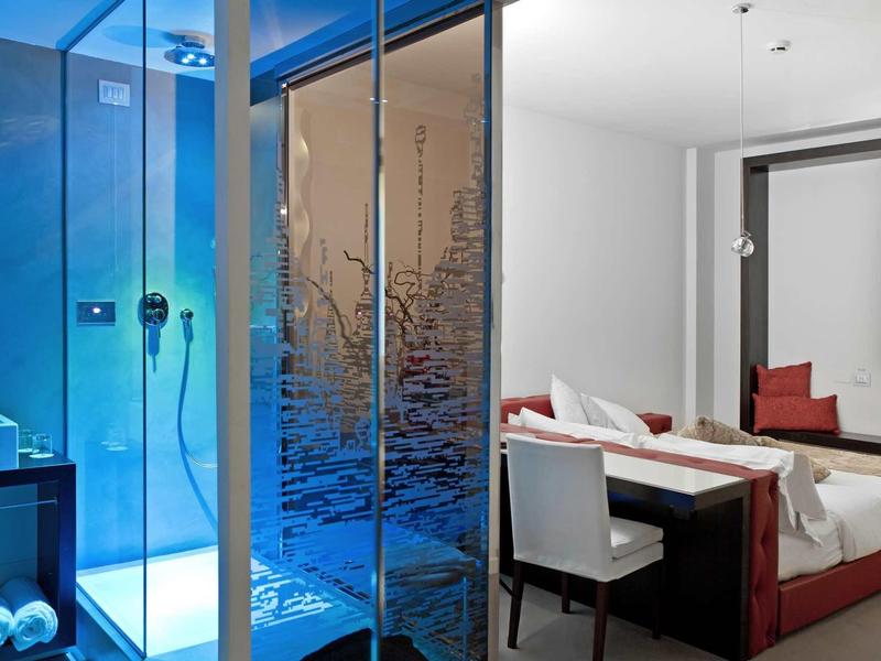 Moderner Hotelzimmerbereich mit Glasduschkabine, Doppelbett und Schreibtisch mit Stuhl.