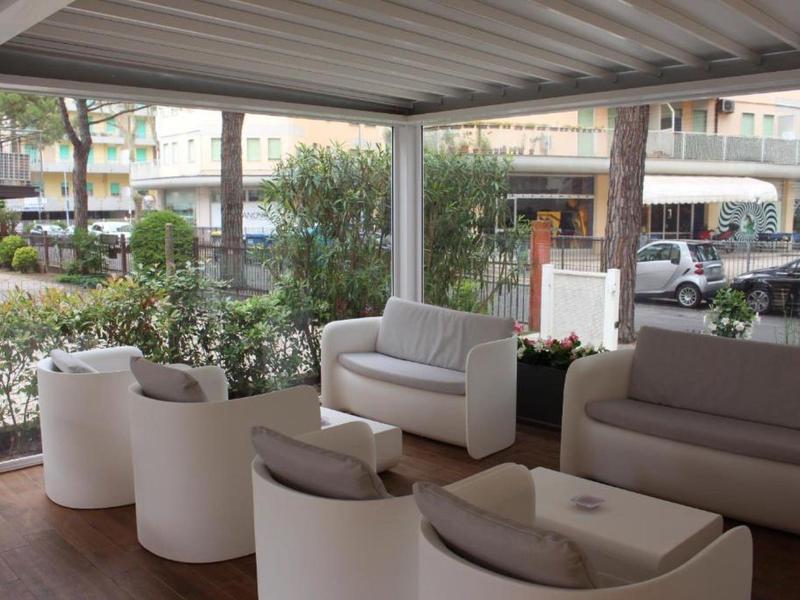 Überdachte Terrasse mit weißen Sesseln und Sofas, Holzboden und Blick auf ein urbanes Umfeld.