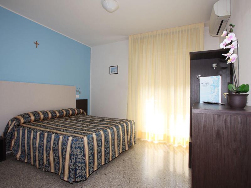 Kleines Schlafzimmer mit blau-weißen Wänden, gestreiftem Bett, Vorhängen und schwarzem Schrank.