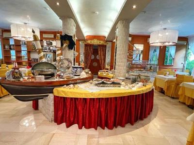 Großer, hell beleuchteter Speisesaal mit buffetförmigem Tisch, gelben Tischdecken und Holzmöbeln.