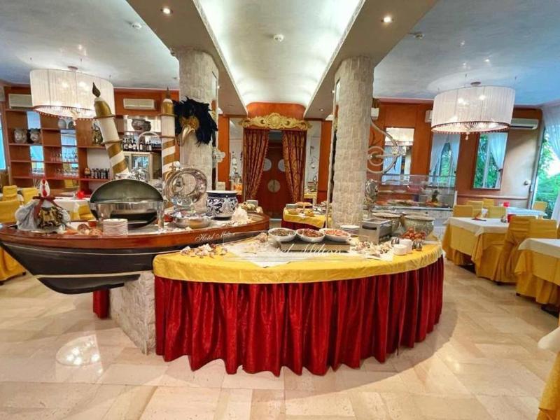 Großer, hell beleuchteter Speisesaal mit buffetförmigem Tisch, gelben Tischdecken und Holzmöbeln.