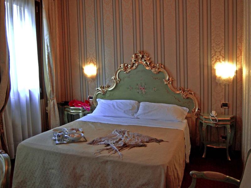Chambre élégante avec tête de lit ornée et éclairage doux près des fenêtres.